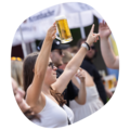 Frau in weißem Top hält Bierkrug hoch und zeigt mit der anderen Hand nach oben