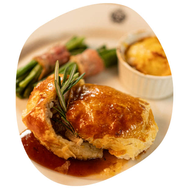 Blätterteigpastete mit Rosmarinzweig und braten Soße, dazu grüner Spargel mit Speck und gratinierte Kartoffeln in kleiner Auflaufform