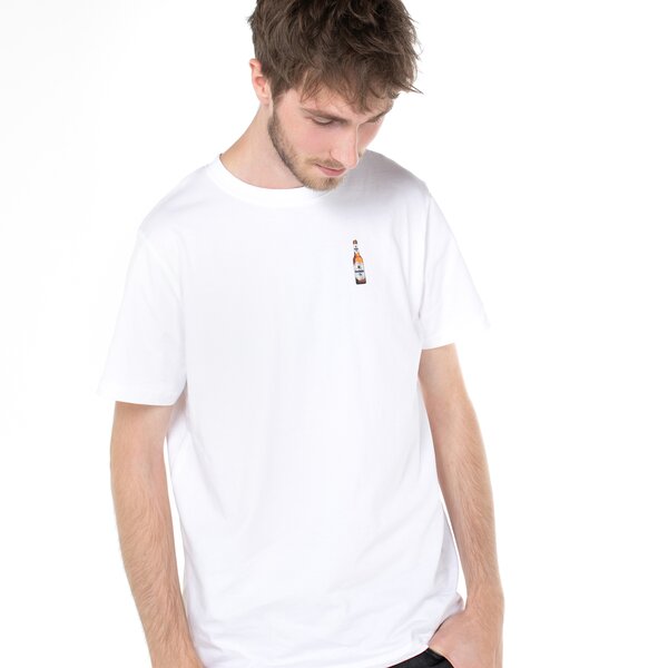 Ein Mann in einem weißen T-Shirt mit Krombacher Pils Flasche auf der Brust, vor einer bunten Wand.