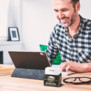 Ein Mann am Schreibtisch mit Büroutensilien und Notizzettelbox in Bierkastenform.