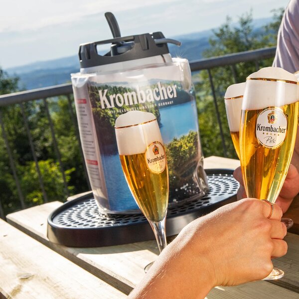 Zwei Hände stoßen mit Gläsern Krombacher Pils an, im Hintergrund steht ein Krombacher Frischefässchen im Icepack.