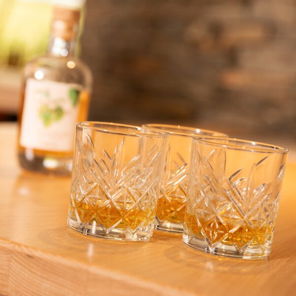 Drei Kristallgläser mit Bierbrand auf einem Holztisch, unscharfer Bierbrand Flasche im Hintergrund.