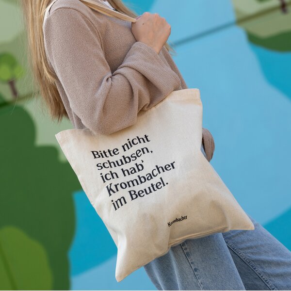 Frau trägt einen hellen Jutebeutel mit dem Text 'Bitte nicht schubsen, ich hab' Krombacher im Beutel.'