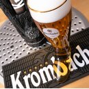Frisch gezapftes Glas Bier in Stiefelform mit Krombacher-Logo, stehend auf einer schwarzen Tropfmatte mit Krombacher-Schriftzug.