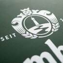 Weißes Krombacher-Logo mit Turm, Hopfen und Gerstenähren auf grünem, strukturiertem Hintergrund, teilweise sichtbarer Schriftzug 'SEIT'.