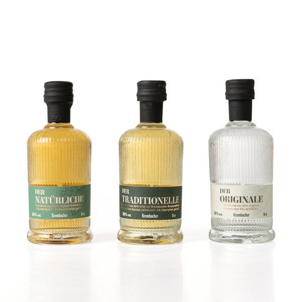 5555_krombachershop_Probierbrand-Set_Produkt_002 Drei kleine Krombacher Probierbrand-Flaschen mit schwarzen Verschlüssen, beschriftet als 'Der Natürliche', 'Der Traditionelle' und 'Der Originale'.