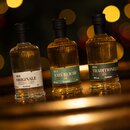 5555_krombachershop_Probierbrand-Set_Mood_001 Drei kleine Krombacher Spirituosenflaschen mit schwarzen Verschlüssen, beschriftet mit 'Der Originale', 'Der Natürliche' und 'Der Traditionelle', vor unscharfem Lichthintergrund.