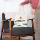 Beige Jutebeutel mit Krombacher-Logo, See und Schriftzug auf dunkelgrauem Sessel mit Holzarmlehnen, Person hält Henkel.