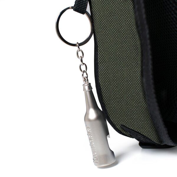 Flaschenöffner in Form einer Flasche aus Metall an grünem Kühlrucksack.