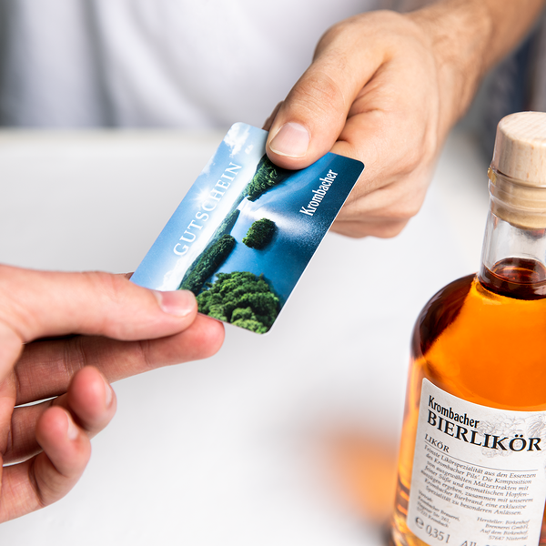 Hand übergibt Krombacher Gutscheinkarte mit Landschaftsmotiv an andere Hand, daneben Flasche Krombacher Bierlikör.